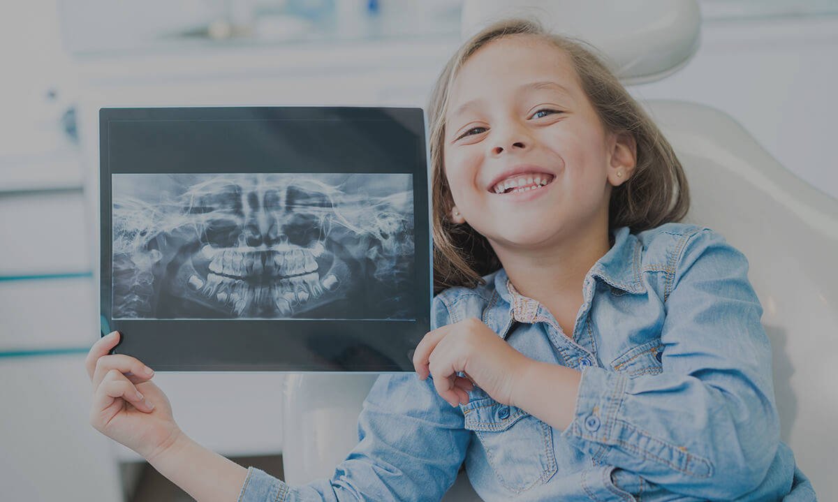 A young patient holding a dental X-ray at Elite Dental